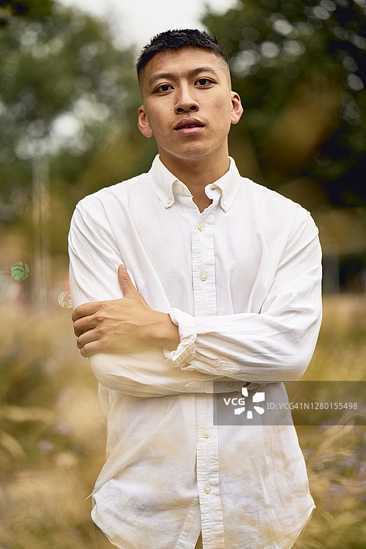 自信地站在城市公园，双臂交叉，身穿白色衬衫的男人图片素材