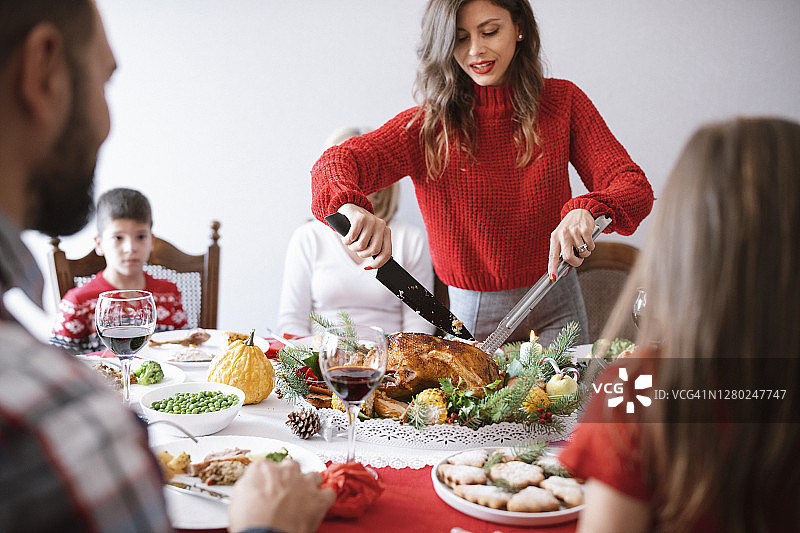 美丽的女人在桌子上为家人和朋友切肉图片素材
