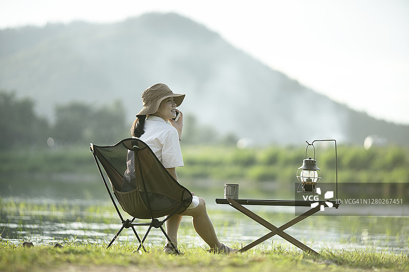 亚洲少女在湖边露营休闲，与朋友通话图片素材