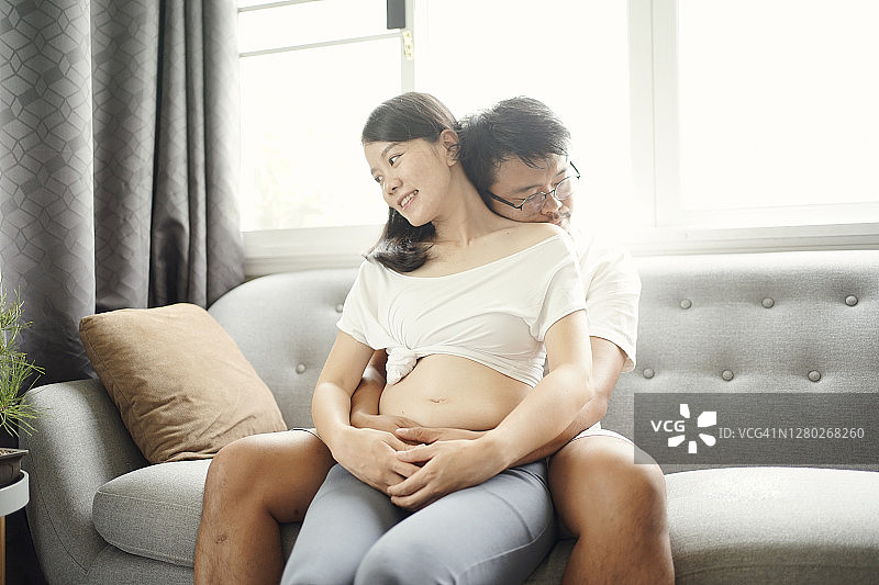 穿着孕妇装的亚洲女性与丈夫感受爱意，触摸腹中新生命图片素材
