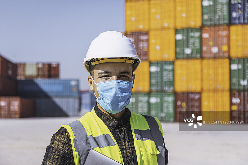 疫情期间戴着医用口罩站在大型商业码头外的物流工程师图片素材