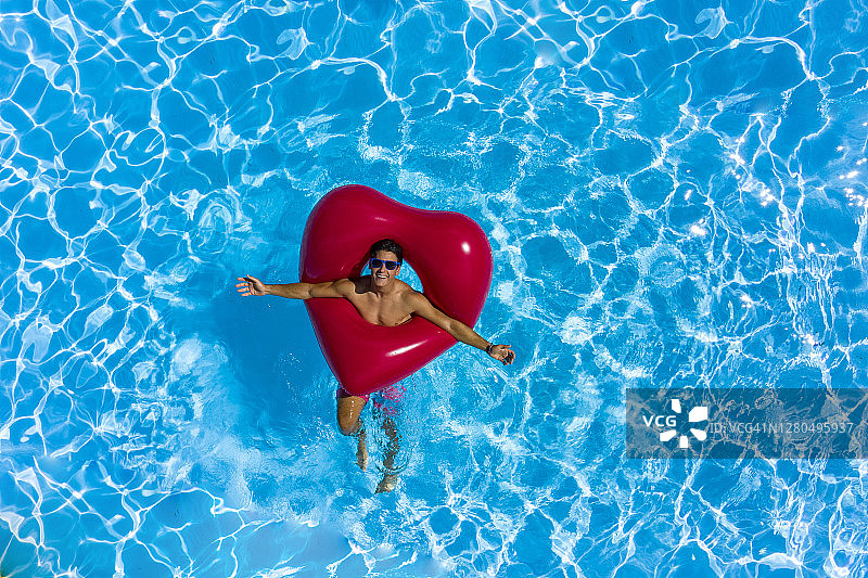 在泳池边拿着红色心形浮标的年轻男人图片素材