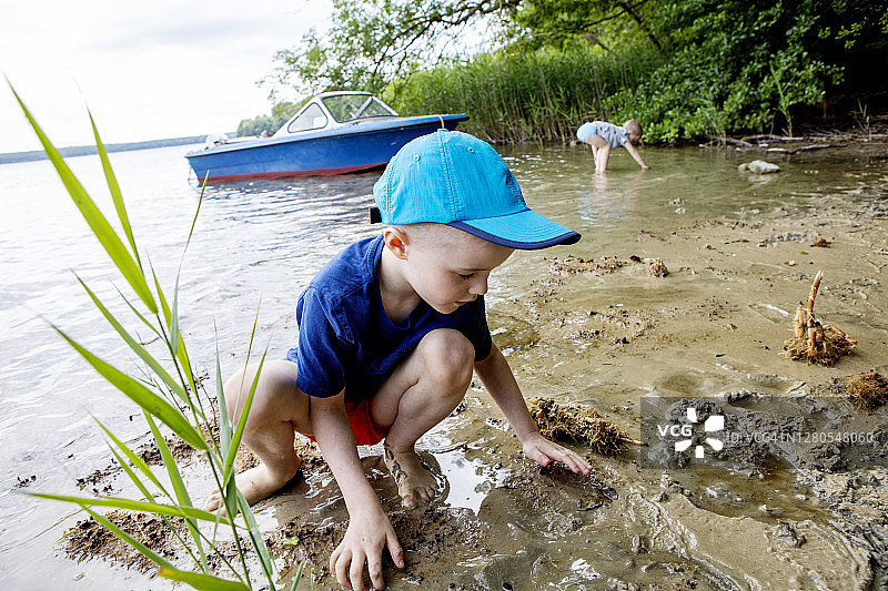 两个男孩在岛上的沙滩上玩耍，有船图片素材