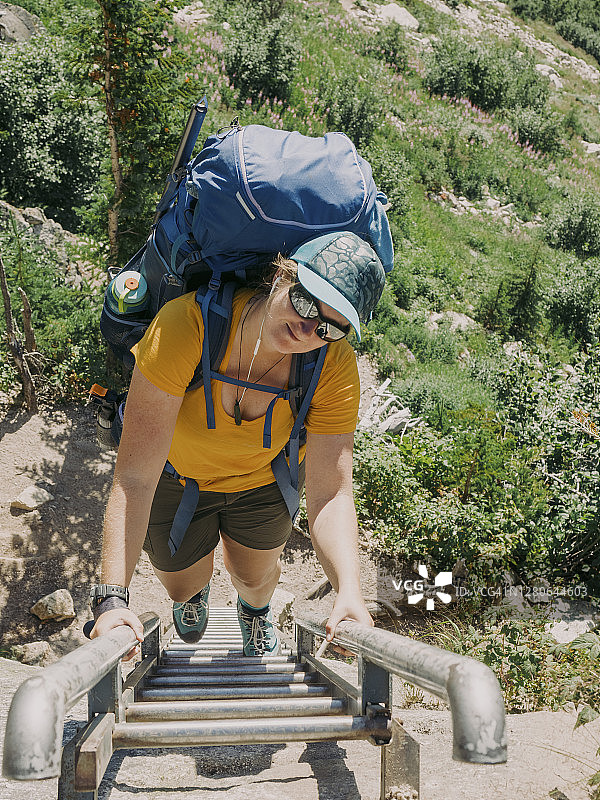 一名妇女背着沉重的大背包，爬上梯子，超越岩石峭壁，徒步进入布加布冰川省立公园图片素材