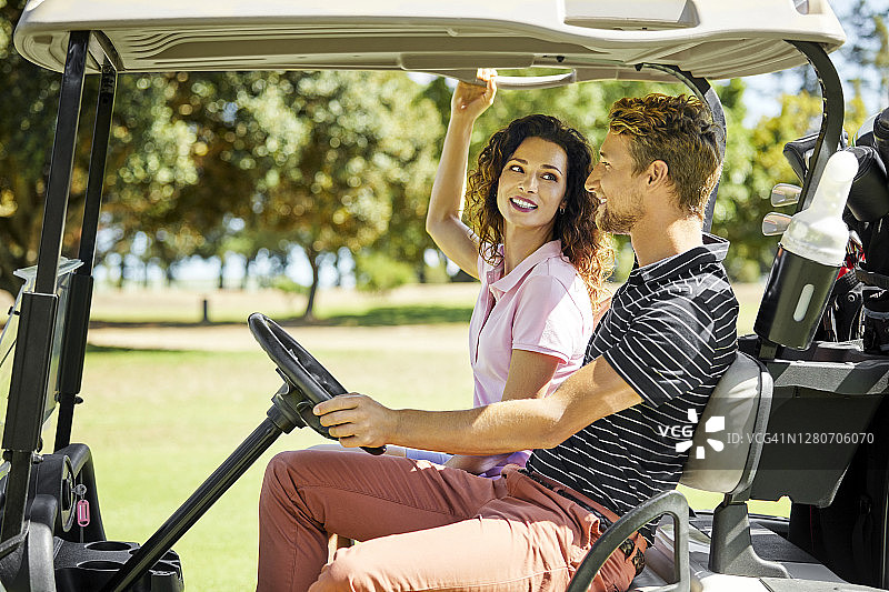 朋友们乘坐高尔夫球车在草地上行驶（侧视图）图片素材