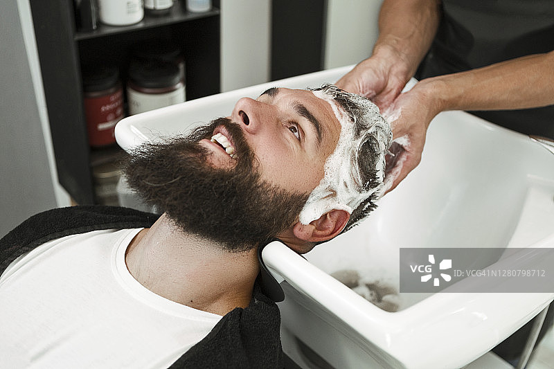 年轻男人在理发店用洗发水洗头图片素材