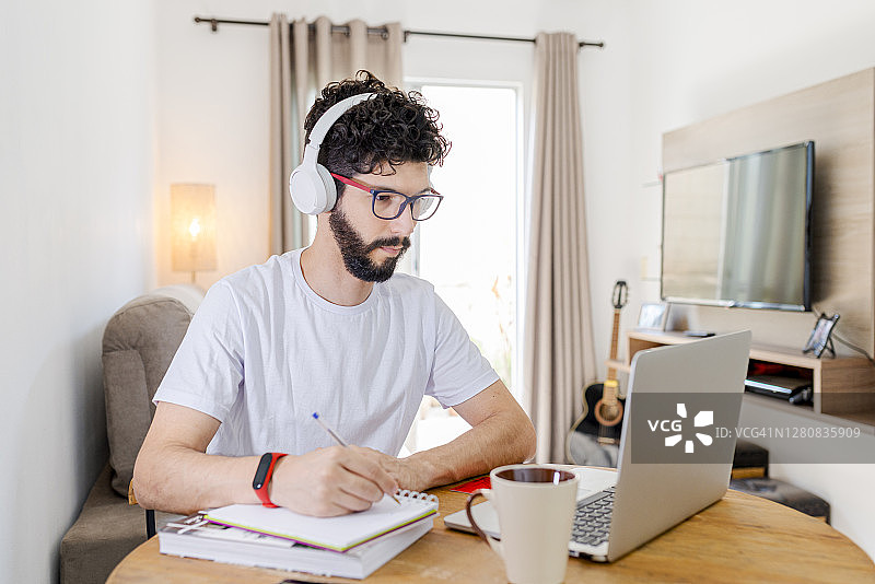 年轻学生在上网课时在笔记本上做笔记图片素材