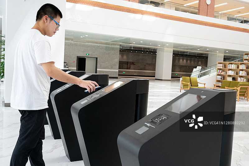 亚洲男人用手机通过检票口。图片素材