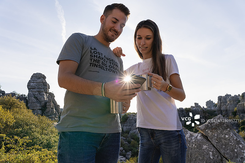 年轻情侣在岩石景观中喝咖啡和使用智能手机图片素材