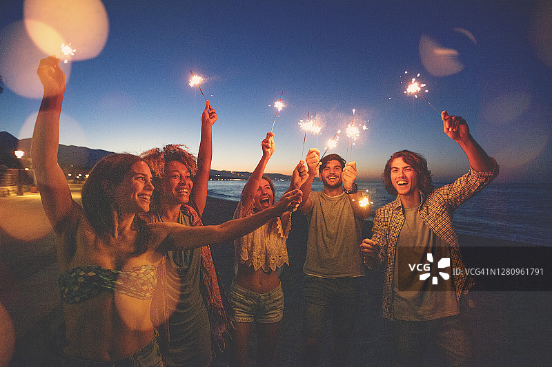 朋友们在日落时分的海滩上玩烟花棒和烟花图片素材