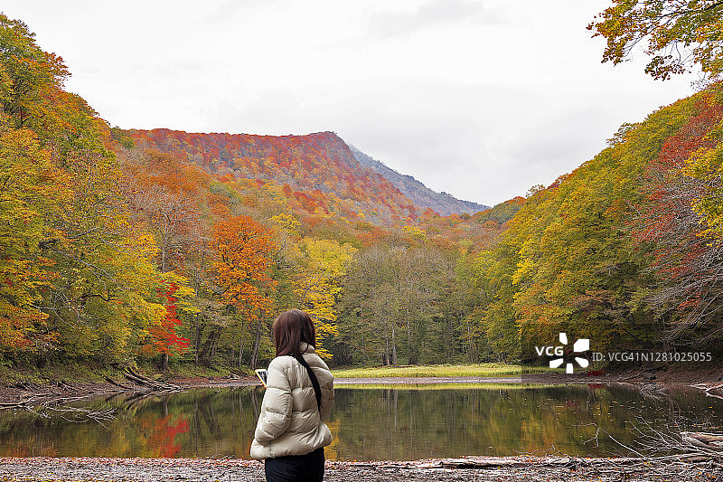 一位东亚女人独自旅行，手持手机，在日本秋季欣赏风景图片素材
