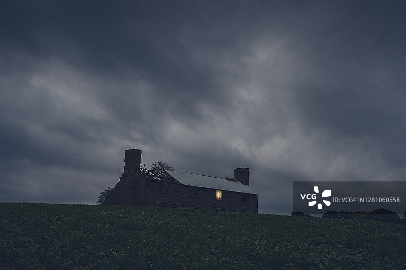 暴风雨夜里，一栋乡村废弃房屋的破窗透出光亮图片素材
