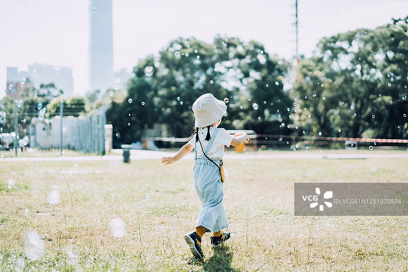 可爱的小亚裔女孩在阳光明媚的公园草坪上玩肥皂泡泡，享受乐趣图片素材