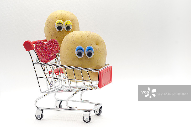 爱与家庭理念：两颗长眼睛的土豆在购物车上，带着红色心形图片素材