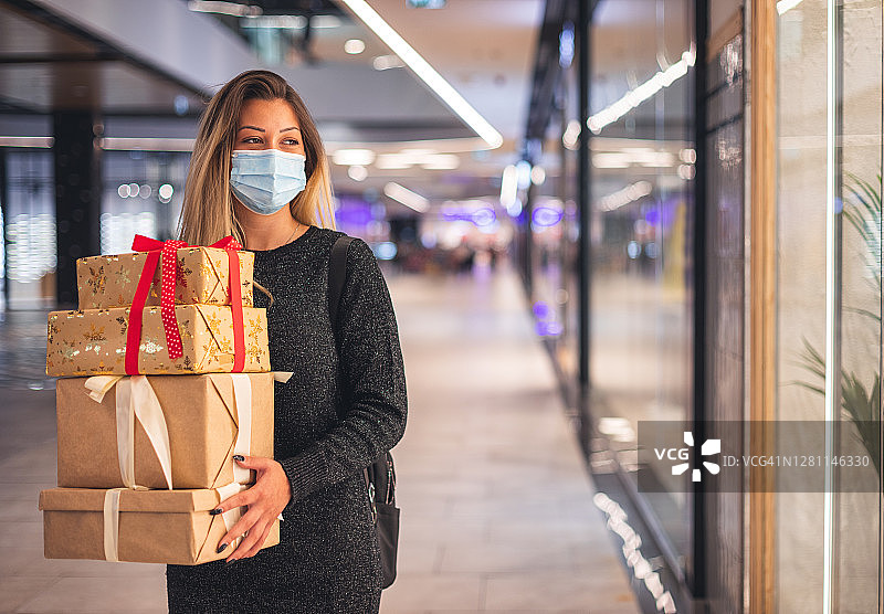 疫情期间在购物中心享受圣诞购物的年轻漂亮女孩。她戴着防护口罩以预防新冠病毒图片素材