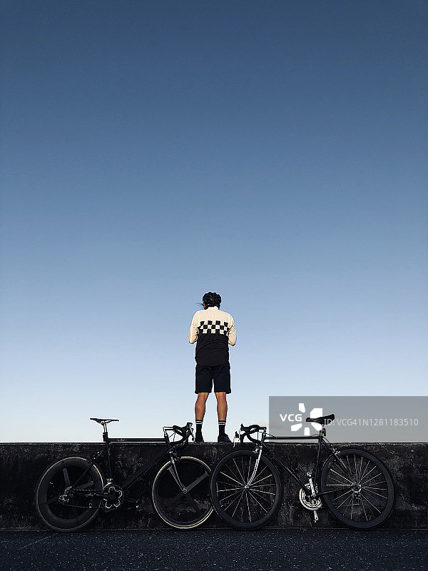 一位年轻的自行车手站在海滩附近，背景是天空和他的自行车图片素材