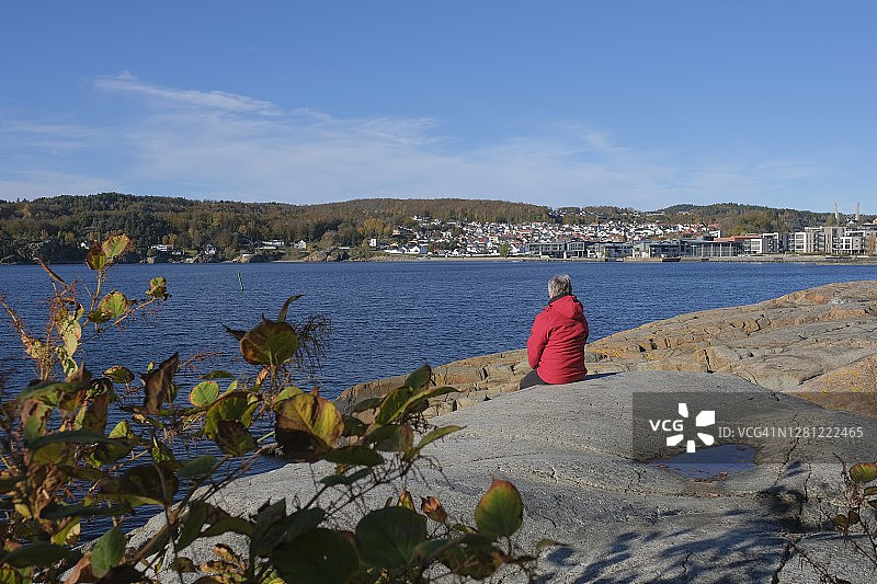 穿红色夹克女人坐在岩石上眺望大海和城市图片素材