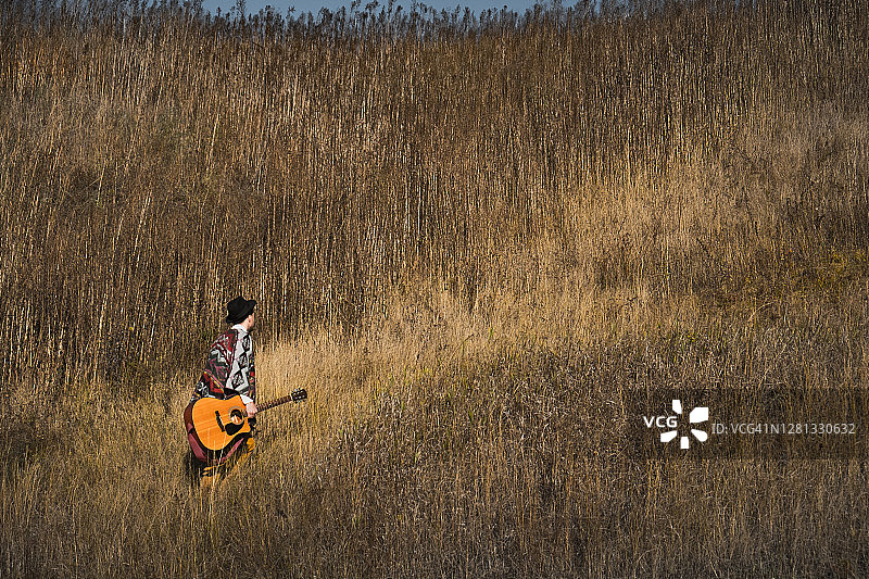 乡村音乐人抱着木吉他在田野的草地上行走图片素材
