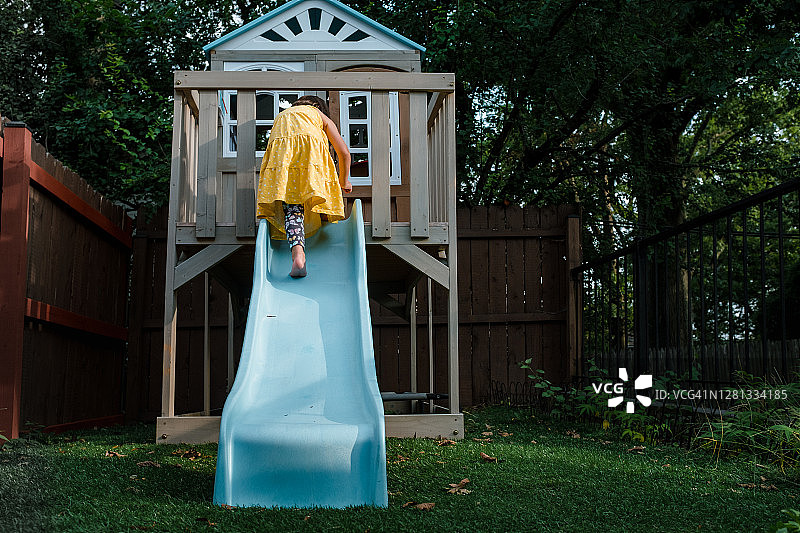 穿着黄色连衣裙的小女孩爬上蓝色滑梯图片素材