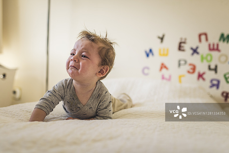在床上哭泣的婴儿，背景是白色毯子和墙上的字母图片素材