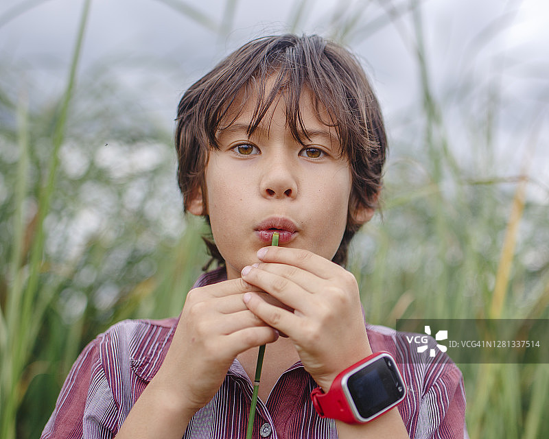 男孩在户外吹空心芦苇演奏音乐的特写图片素材