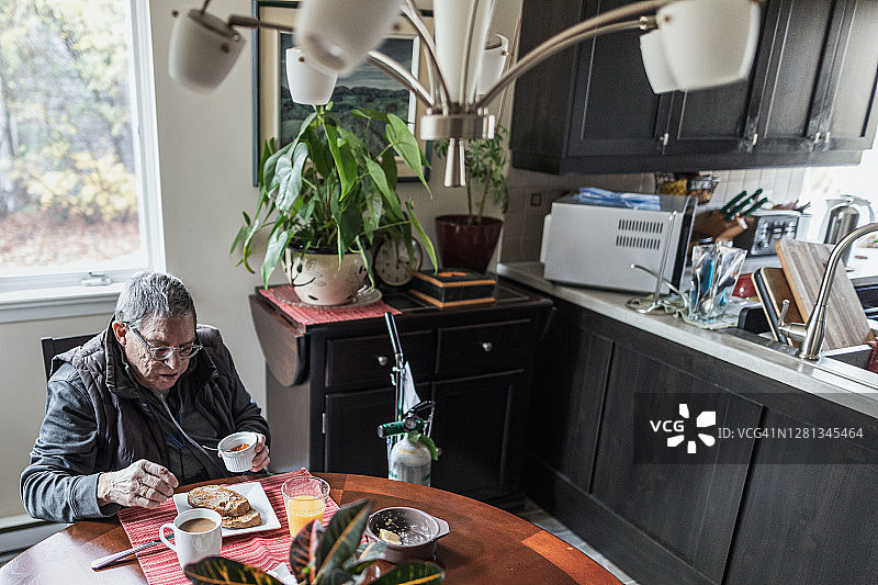 一位独自在桌旁吃早餐的年长男人图片素材