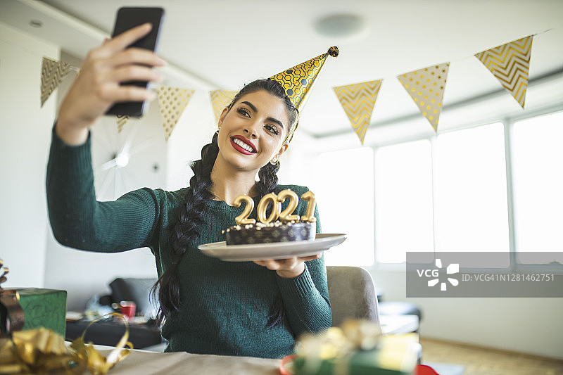 年轻女子新年视频通话，制作蛋糕和包装礼物图片素材