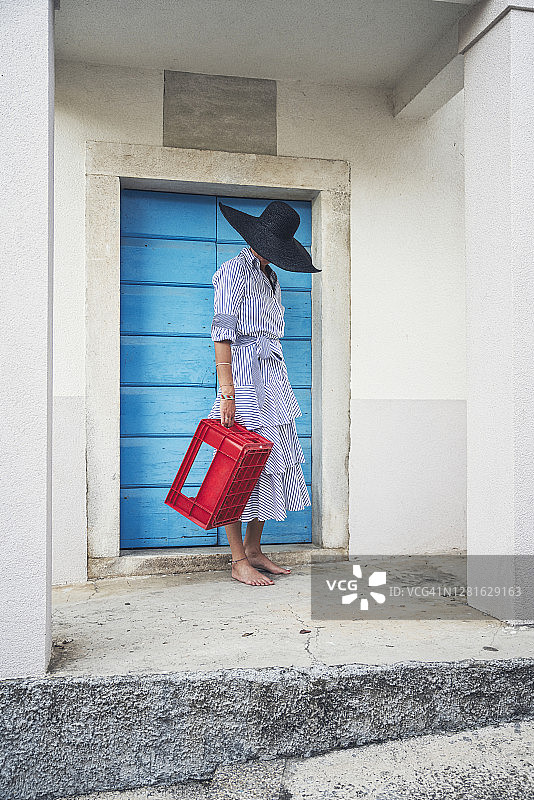 在老城区，漂亮的女人在绿松石色的门前摆姿势，手持红色箱子图片素材