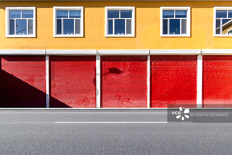 明黄色墙壁上的红色卷帘门图片素材