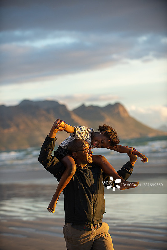 日落沙滩上，女儿坐在爸爸的肩头一起欢笑图片素材