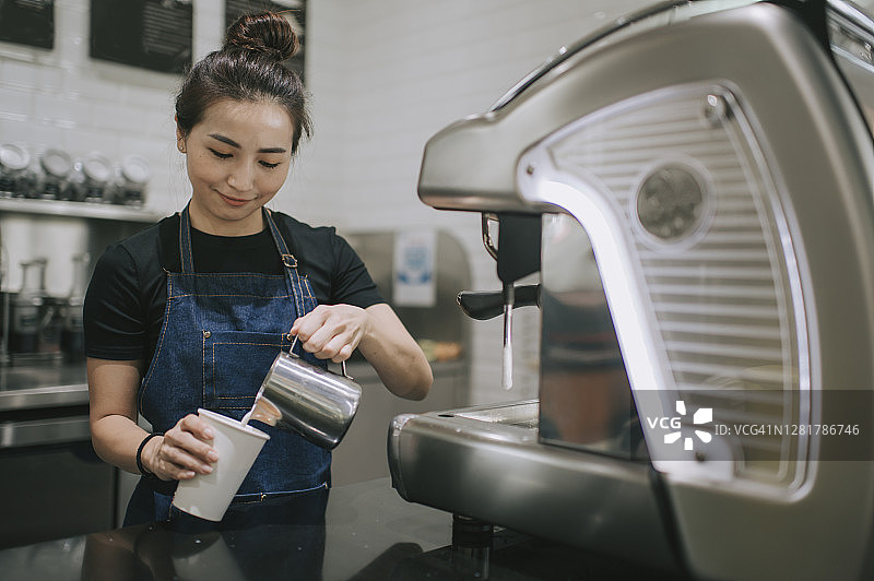 中国咖啡师在咖啡馆用咖啡机制作咖啡并倒入牛奶图片素材