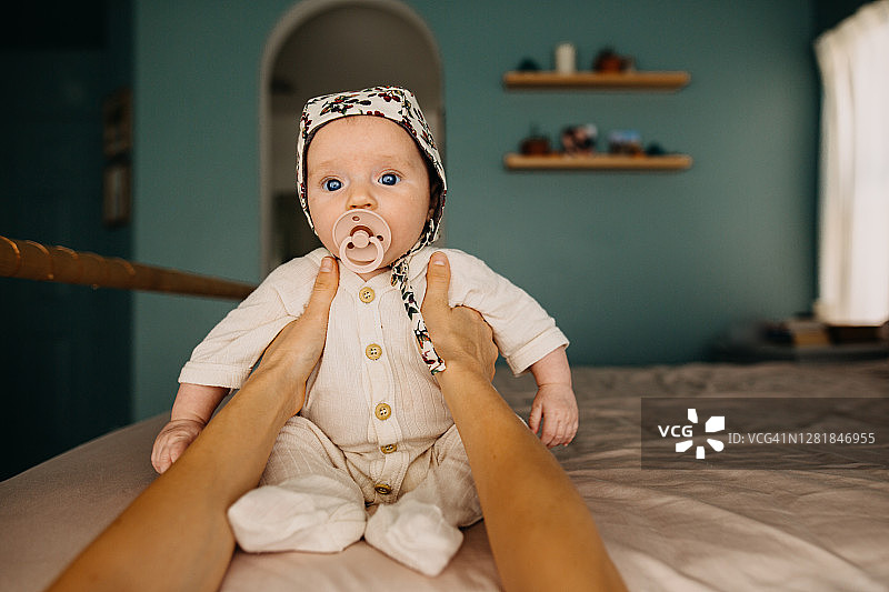 在母亲帮助下坐在床上的戴着睡帽的婴孩图片素材