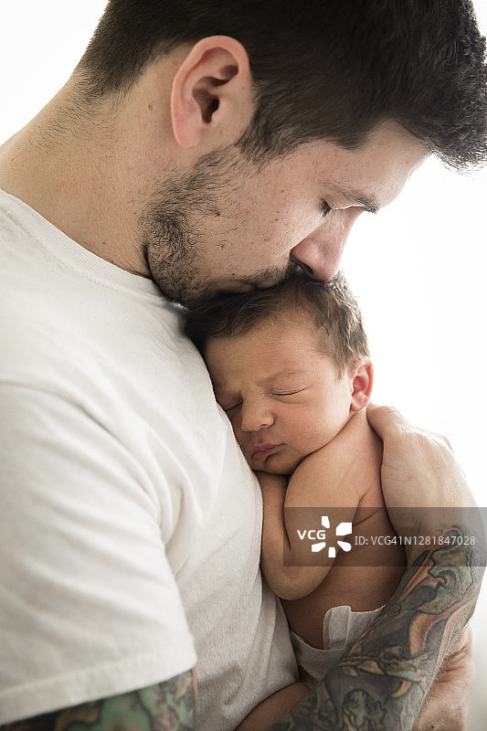 有纹身的千禧一代父亲亲吻新生儿子的侧面特写图片素材