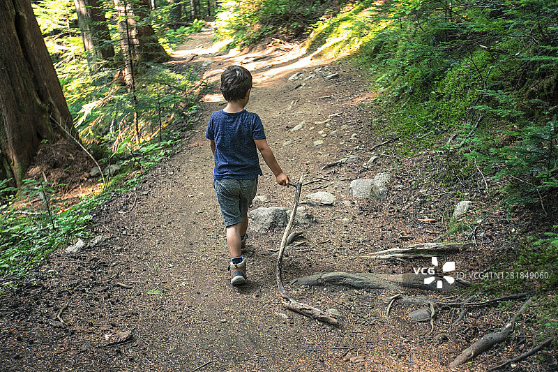 男孩拿着树枝在自然小径上行走图片素材