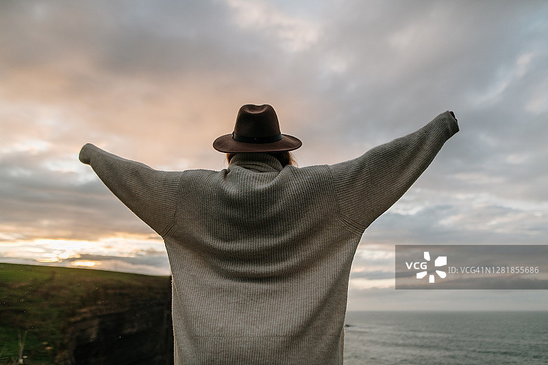 在美丽日落天空下举起双臂的年轻女人图片素材