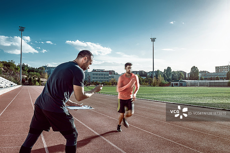 在田径跑道上进行训练的跑步者和教练，教练用秒表测量结果图片素材