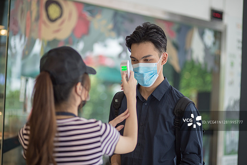 咖啡馆员工使用红外线测温仪为顾客测量体温。新常态概念。新冠病毒 Covid-19 预防发热检查图片素材
