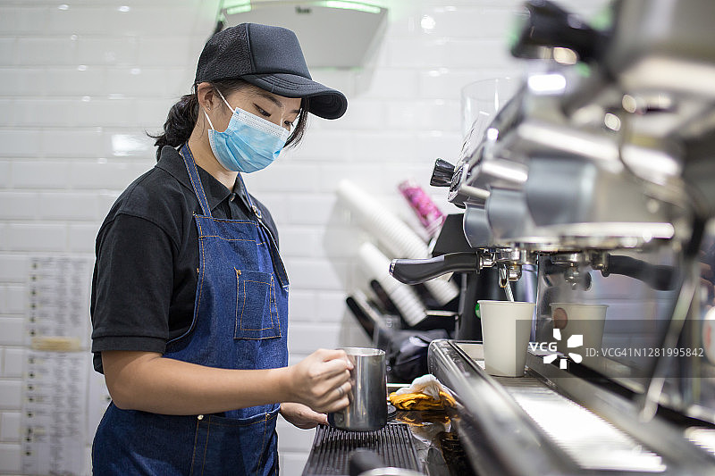 戴口罩的中国女咖啡师在咖啡馆用咖啡机制作咖啡图片素材