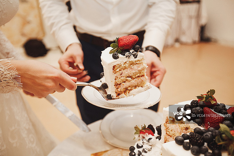 新娘和新郎在白色木桌上切开装饰有浆果的精致双层结婚蛋糕图片素材