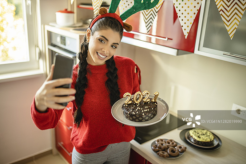 漂亮女人庆祝圣诞节，进行视频通话并手持2020数字造型的巧克力蛋糕，迎接新年图片素材