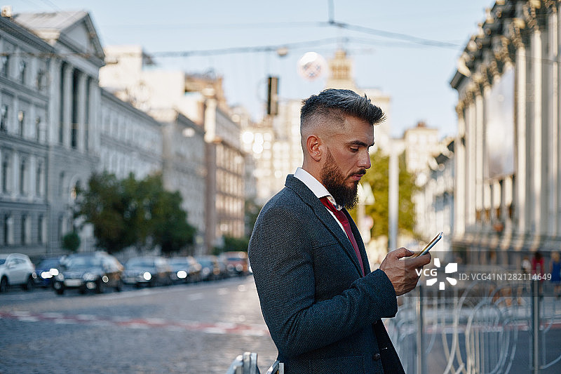 日落时分在城市街道上用手机的商务西装中年男商人图片素材