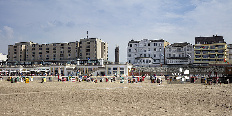 戴帽衫的人在阳光明媚的海滩上，城市建筑背景图片素材