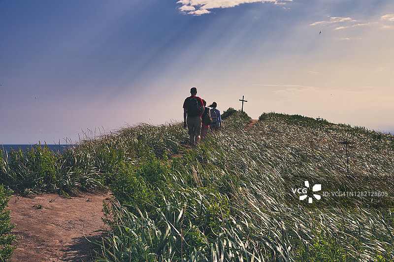 日落时分，朋友们在山顶的植物中徒步前往山顶十字架图片素材
