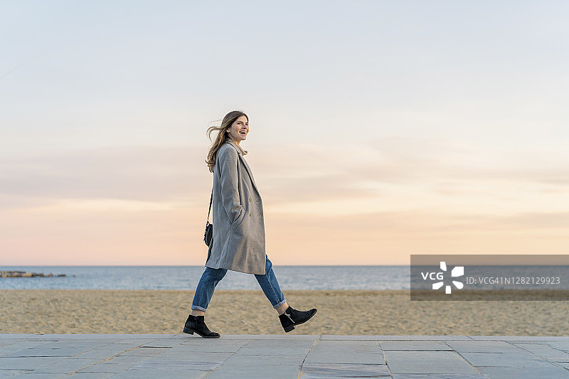 快乐美丽的女人在海滩长廊上行走，日落时分眺望天空图片素材