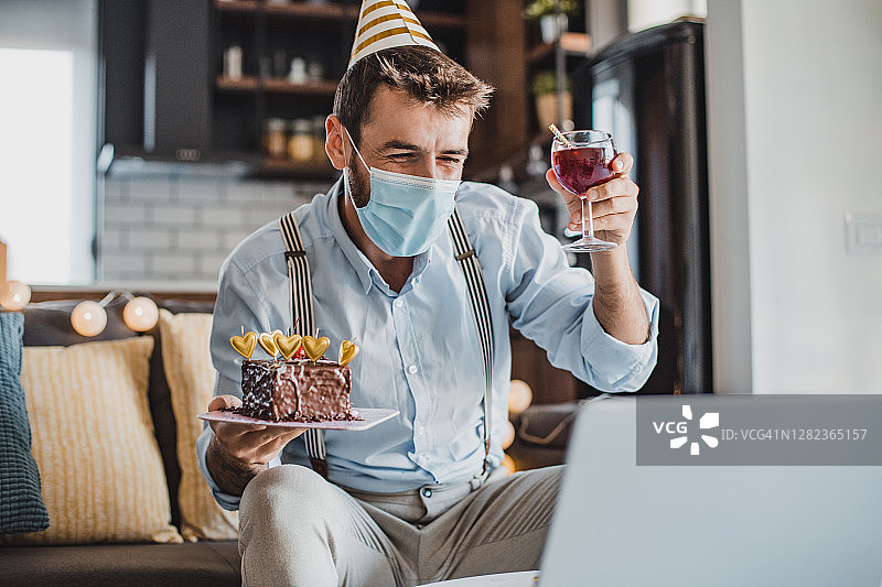 戴口罩的年轻男人在家中视频通话庆祝生日图片素材