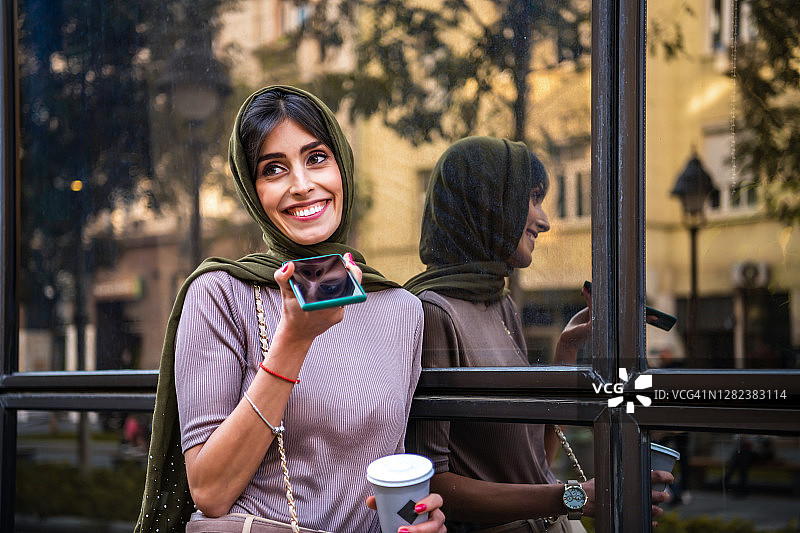 美丽的穆斯林妇女在街上打电话喝咖啡图片素材