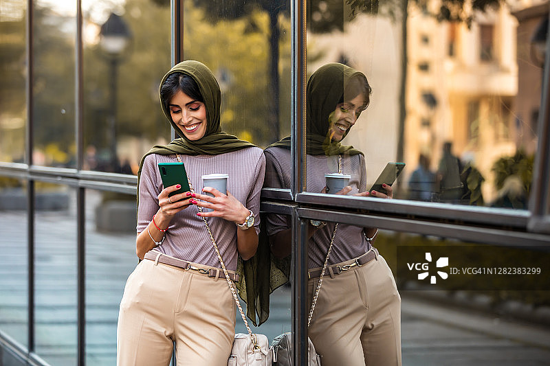 正在智能手机上打字并拿着咖啡杯的穆斯林中年妇女图片素材