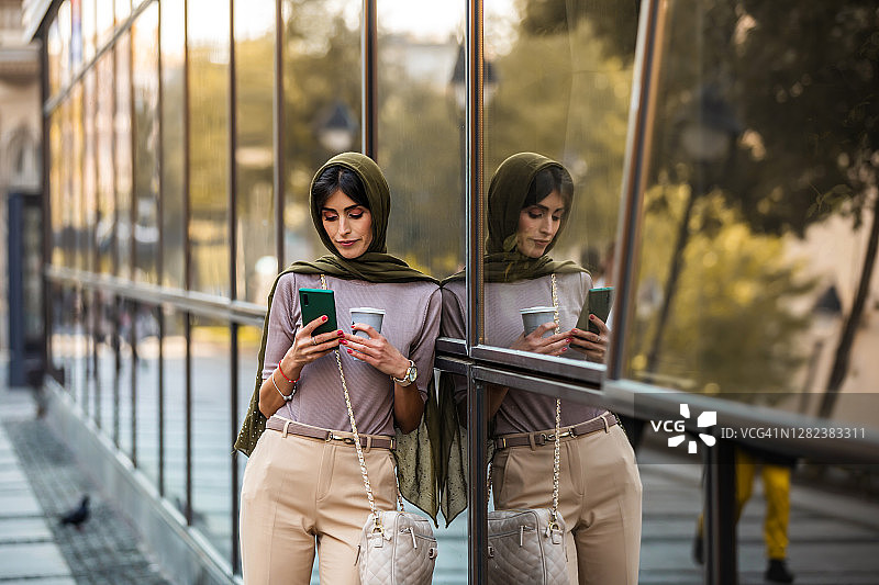 中年阿拉伯妇女在街头使用手机喝咖啡的肖像图片素材