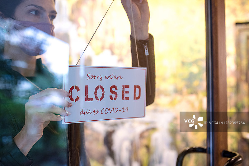 年轻女子在商店门上挂“停止营业”的牌子图片素材
