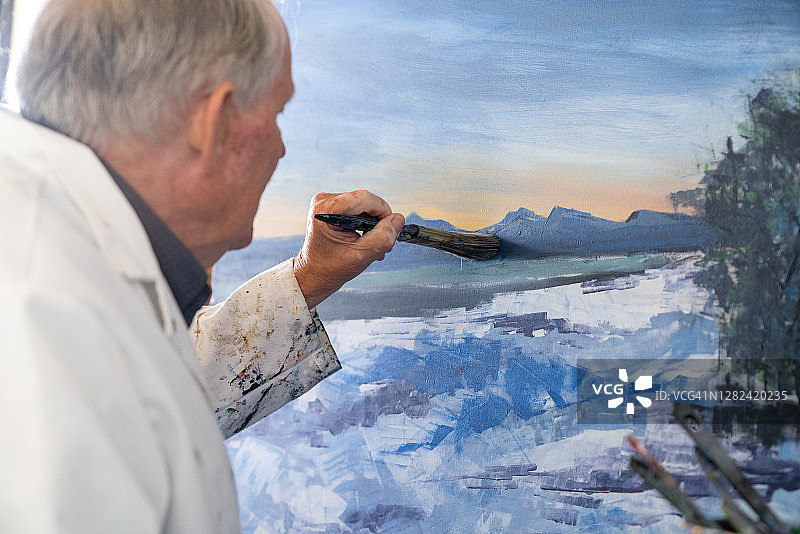 在工作室绘画的年长男艺术家，坐在画前工作图片素材